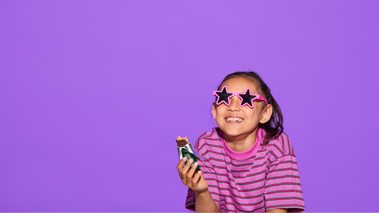 Child wearing pink sunglasses and holding a phone against a purple background
